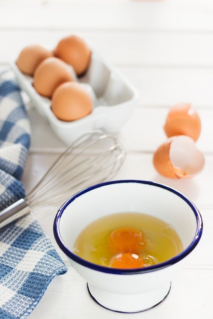 Aufgeschlagene Eier in Emailleschüssel und ganze Eier im Eierkarton
