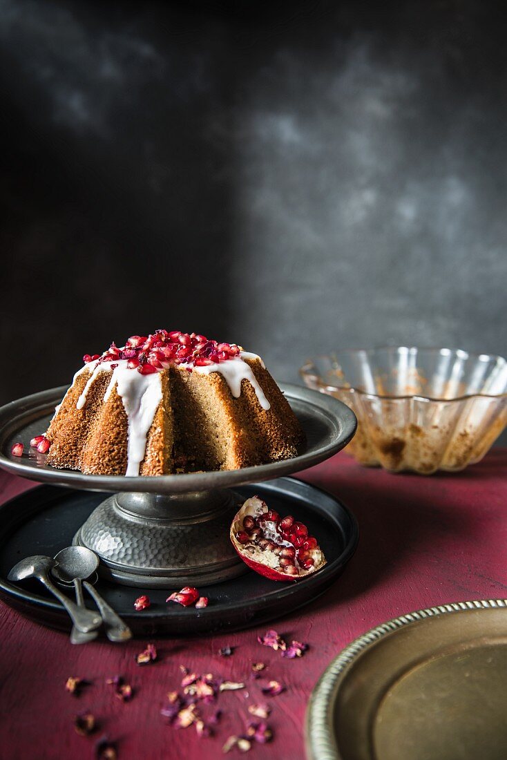 Pomegranate and rosewater cake with icing on a metal cake stand