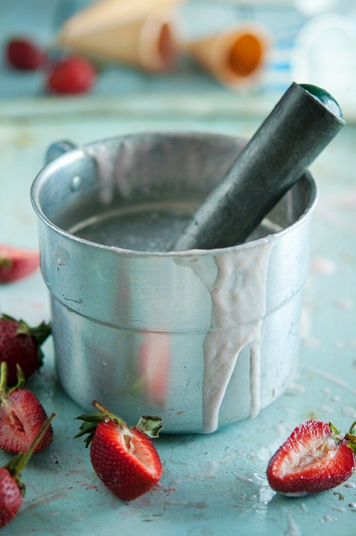 An ice cream scoop in a pot of water with fresh strawberries and ice cream cones