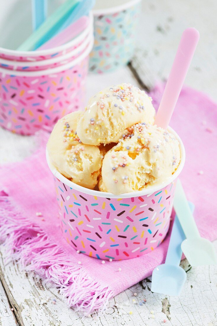 Vanilla ice cream with sugar sprinkles in a pink paper tub