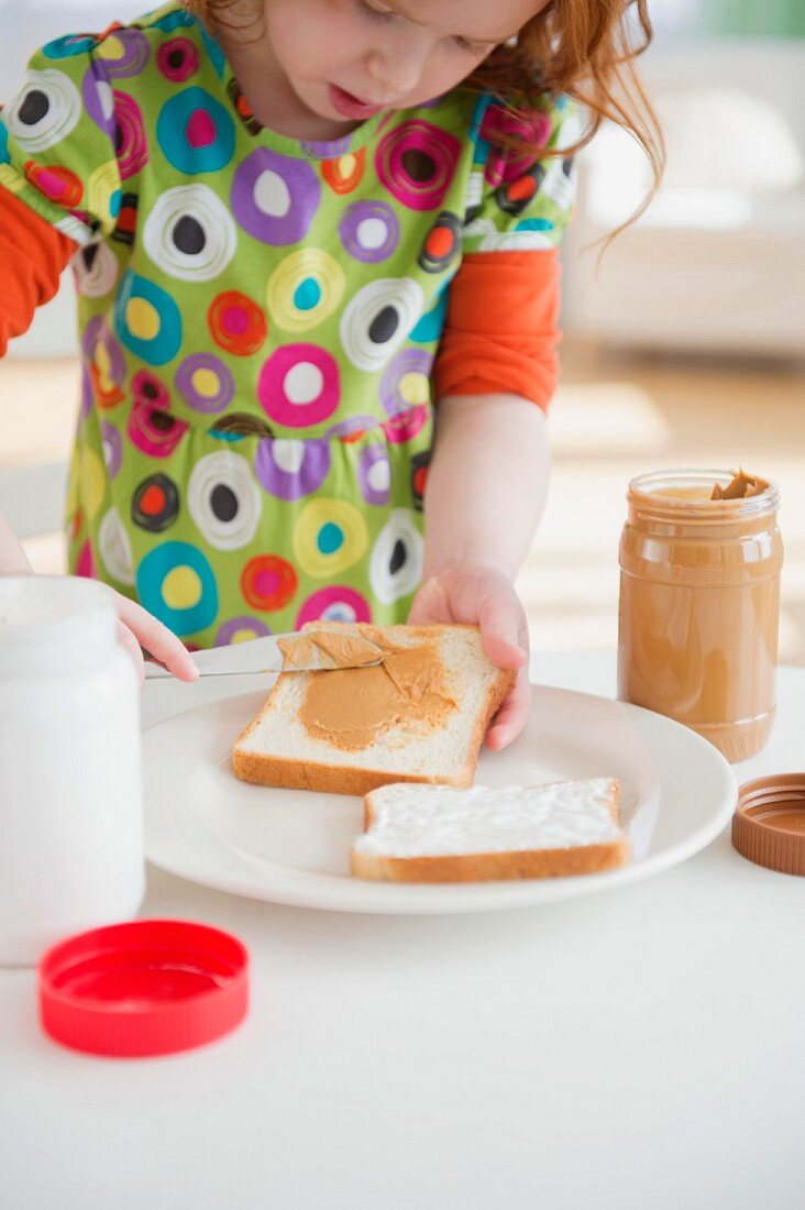 Mädchen streicht Erdnusscreme auf Toastscheibe