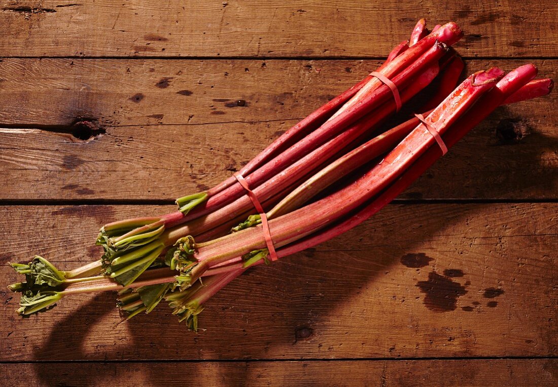 Two bunches of fresh rhubarb stalks on a wooden surface