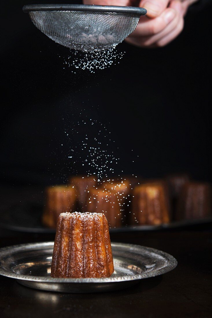 A cannelle being dusted with icing sugar