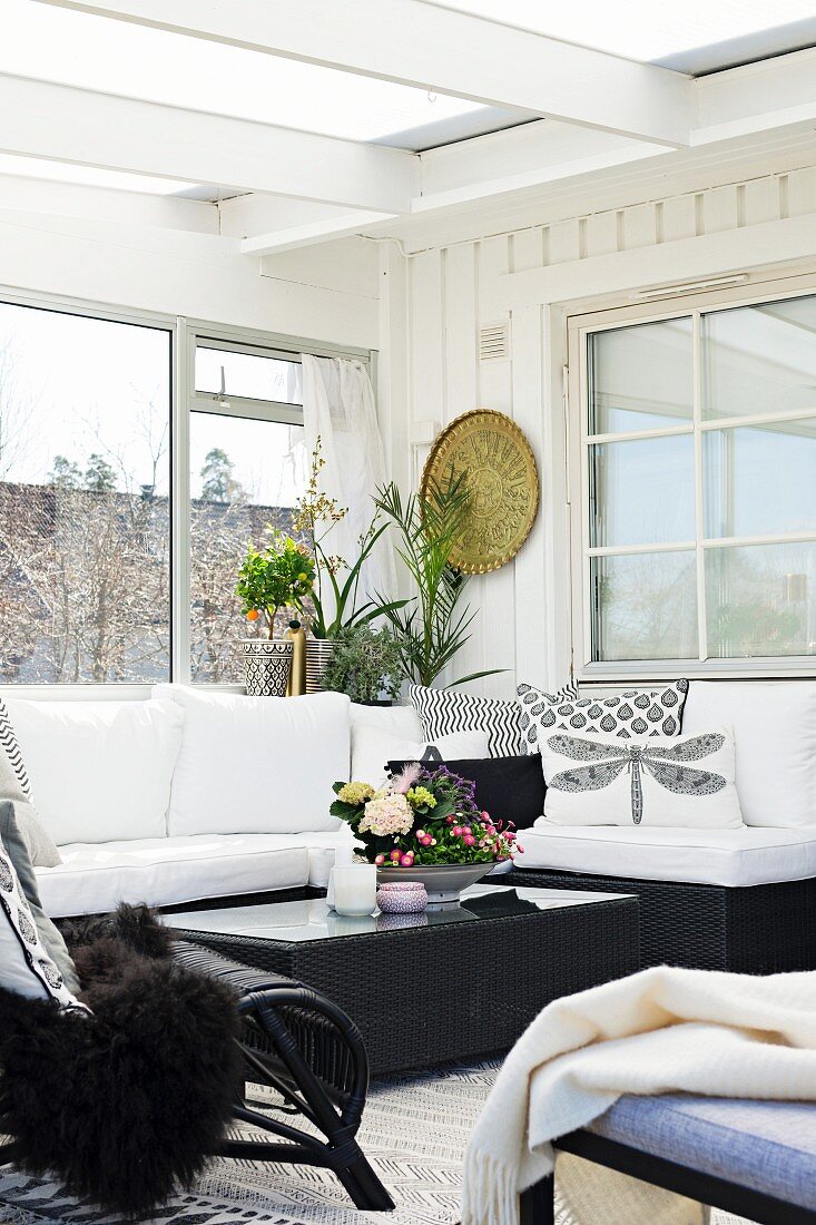 Black wicker coffee table and comfortable couch in conservatory extension with Scandinavian ambiance