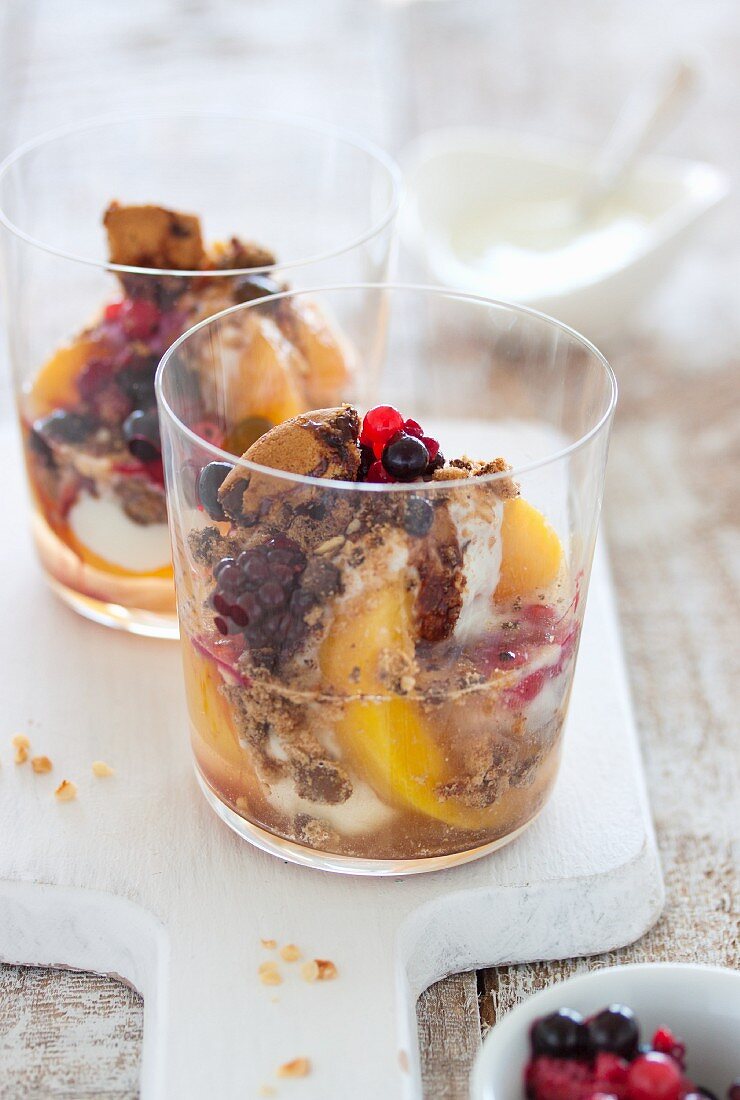Yoghurt dessert with peaches, berries, biscuits and syrup