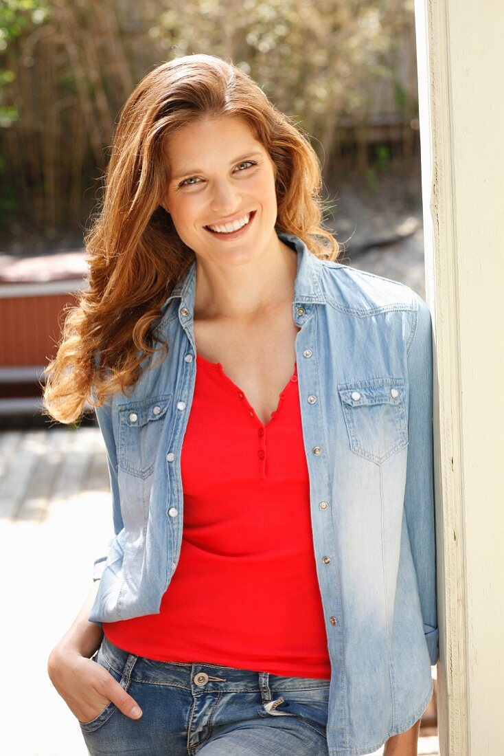 A young brunette woman wearing jeans, a red top and a denim blouse