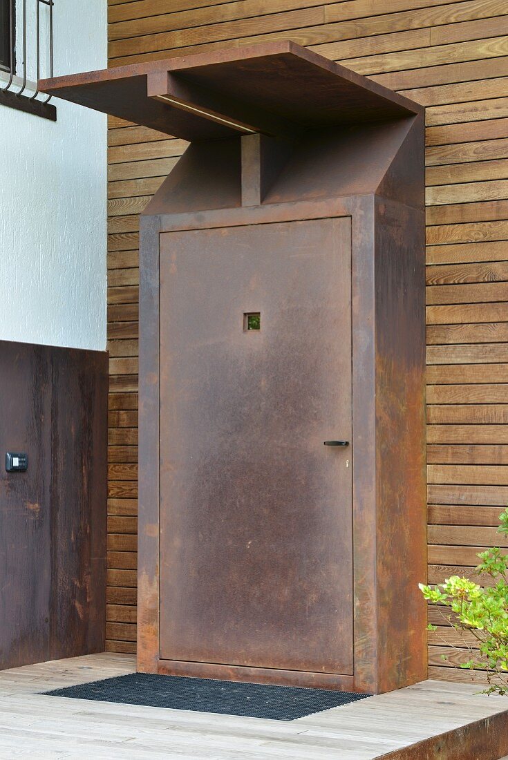 Rusted front door and porch on wood-clad façade