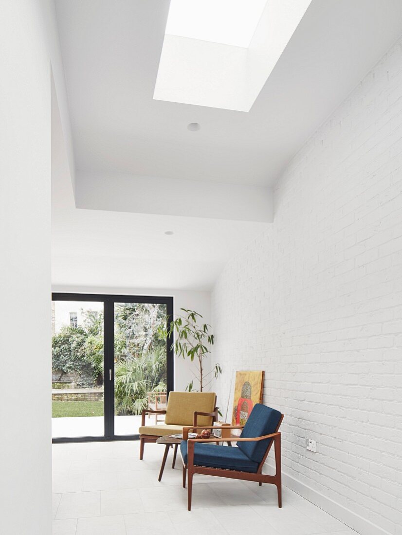 Blue and yellow, 50s retro armchairs with wooden frames against white brick wall in modern interior