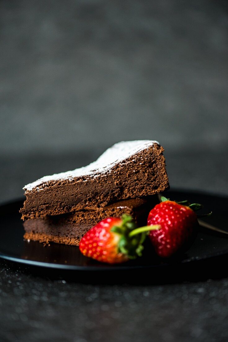A slice of chocolate cake with icing sugar and strawberries