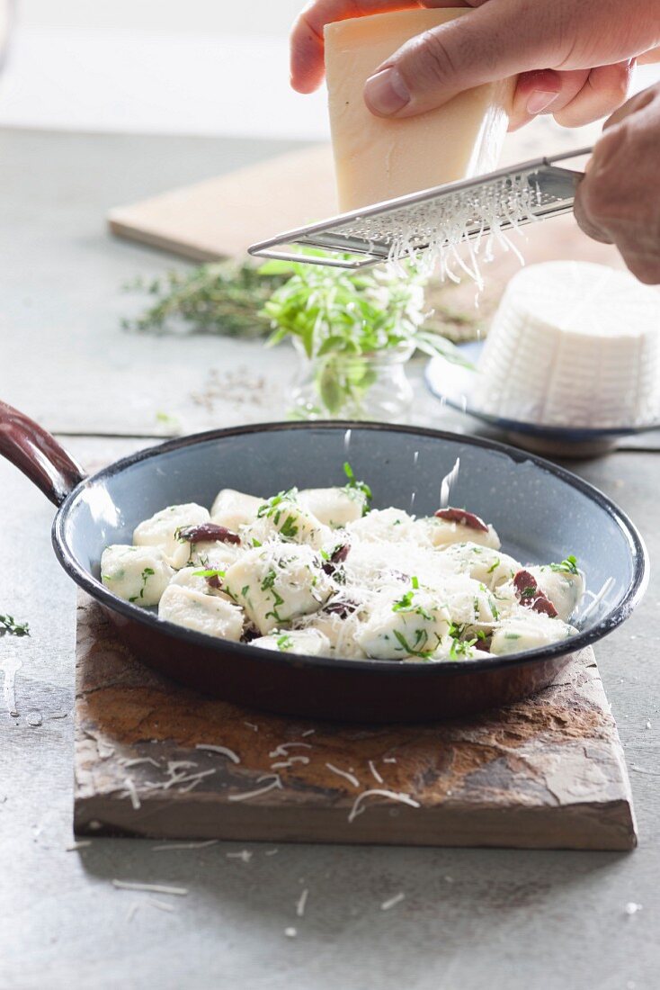 Parmesan wird über Gnocchi mit Ricotta und Kräutern gerieben