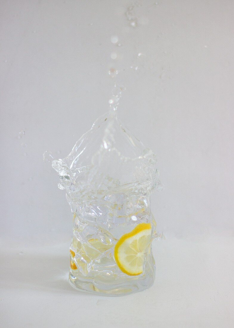 Ein spritzender Gin Tonic im Glas vor weißem Hintergrund