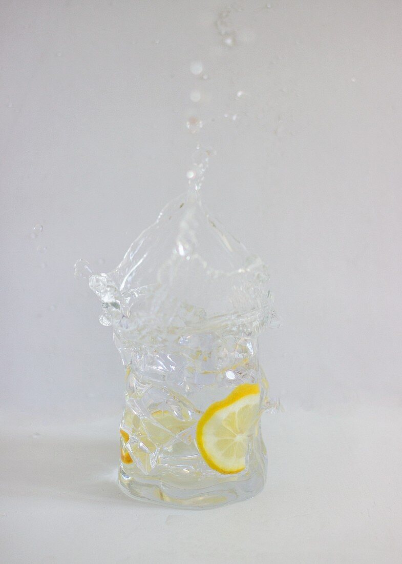 Gin and tonic splashing out of a glass against a white background