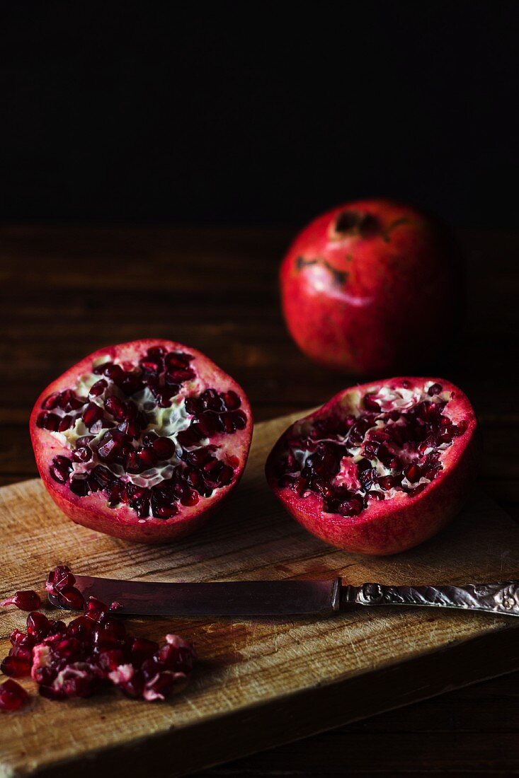 A halved pomegranate on a wooden chopping board