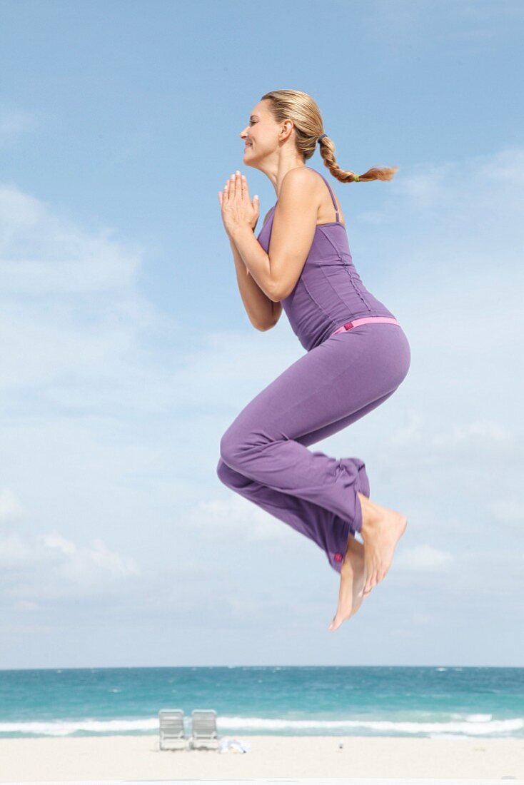 A young blonde woman wearing sports clothes exercising on a beach