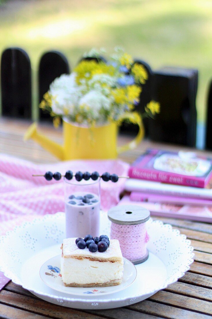 A cream slice and a milkshake with blueberries on a summer table outside