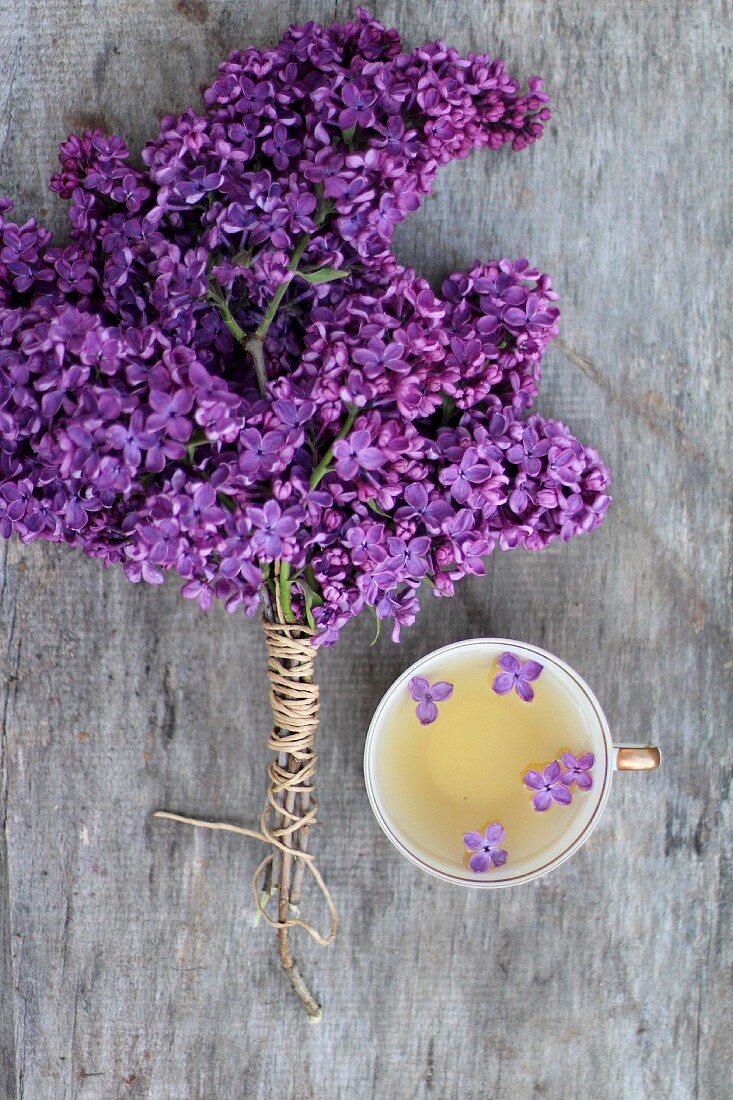 Bund mit violetten Fliederblüten neben Tasse Tee mit Fliederblüten