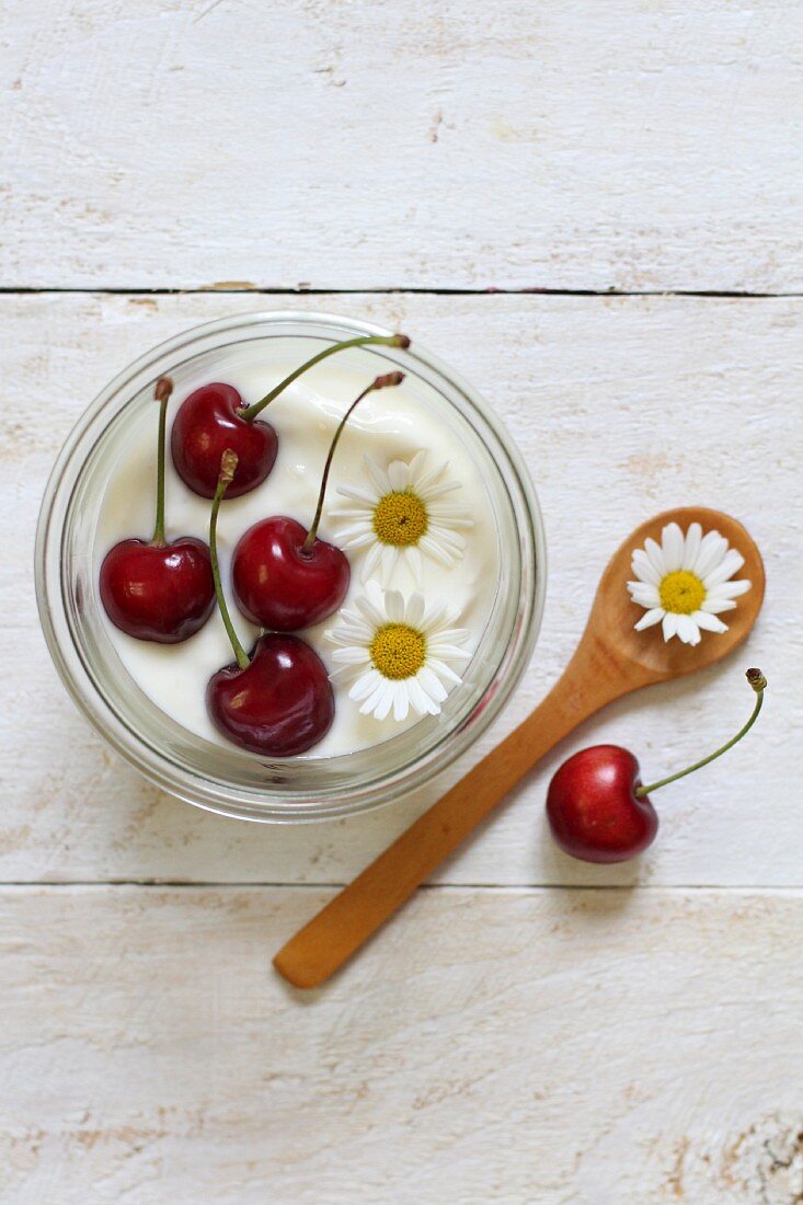 Yoghurt garnished with cherries and daisies (seen from above)