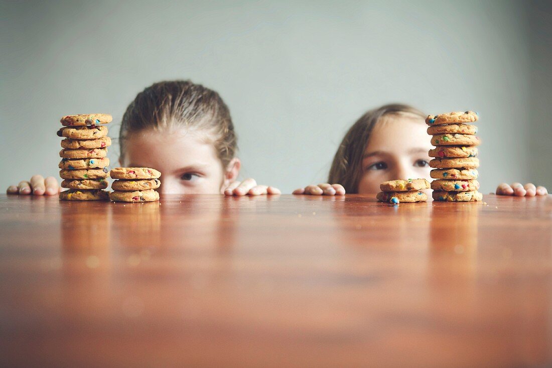 Zwei Mädchen schauen über Tischrand auf Keksstapel