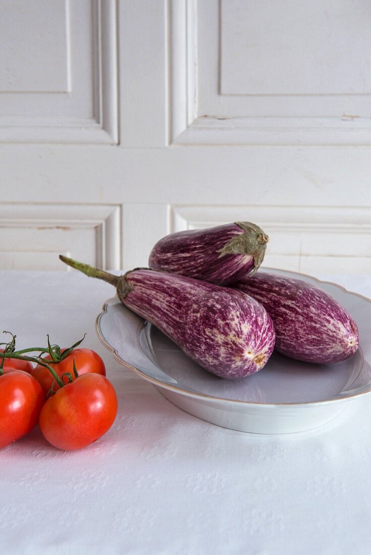 Aubergines on a porcelain plate next to tomatoes