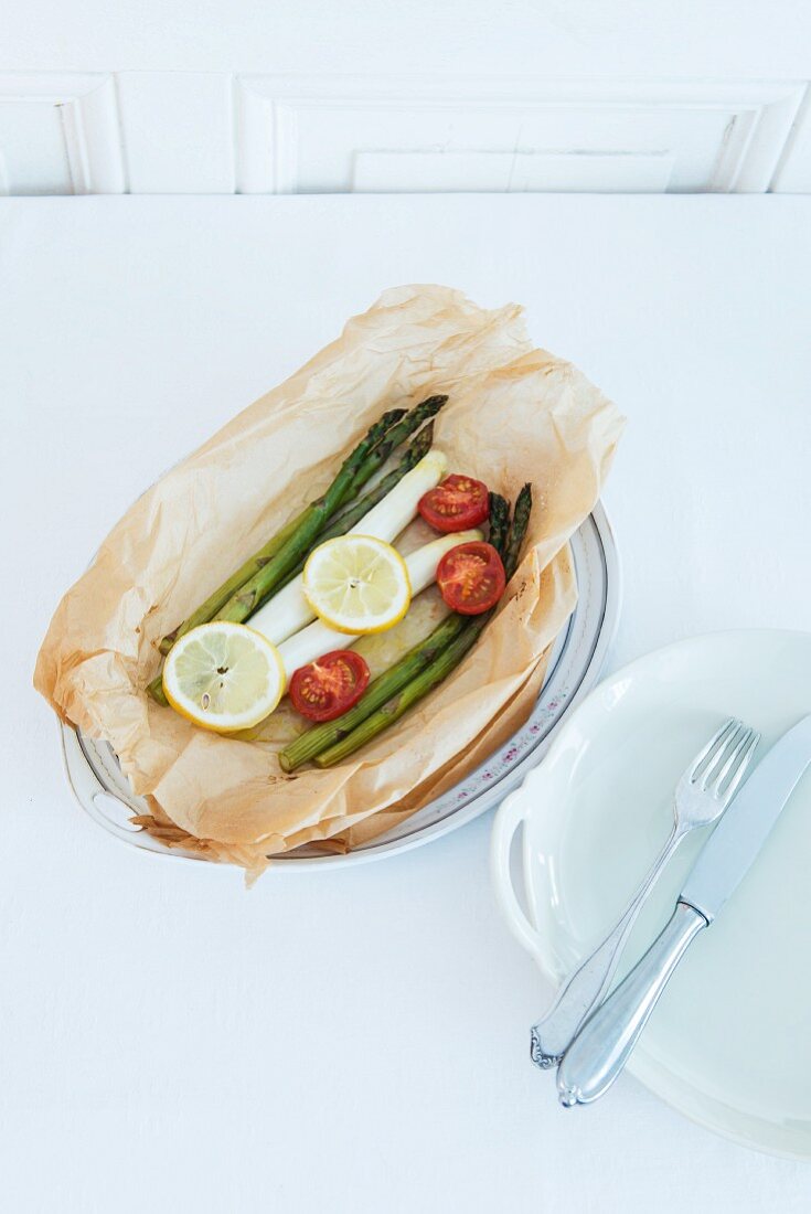Green and white asparagus in baking paper with cocktail tomatoes and lemon
