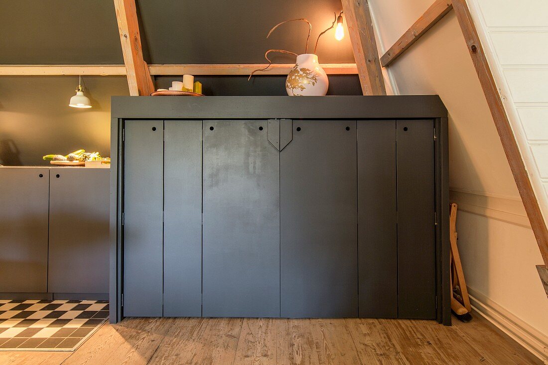 Half-height fitted cupboards painted dark grey under sloping ceiling with exposed wooden roof beams