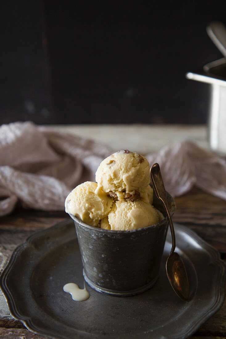 Scoops of rum and raisin ice cream in a metal cup on a pewter plate