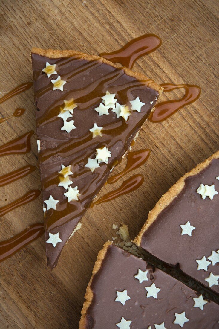 Tarte Au Chocolat mit kleinen weißen Sternchen und Karamellsauce auf Holzbrett