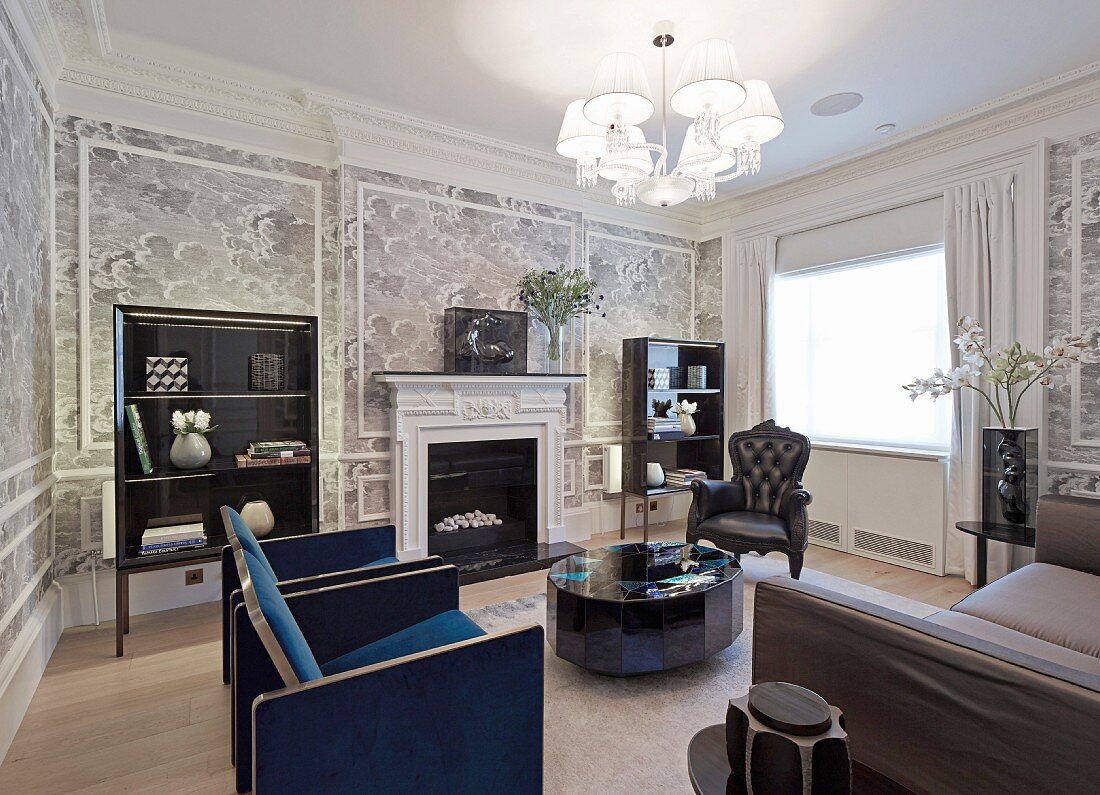 Elegant armchairs around round coffee table in front of open fireplace in grand, traditional lounge