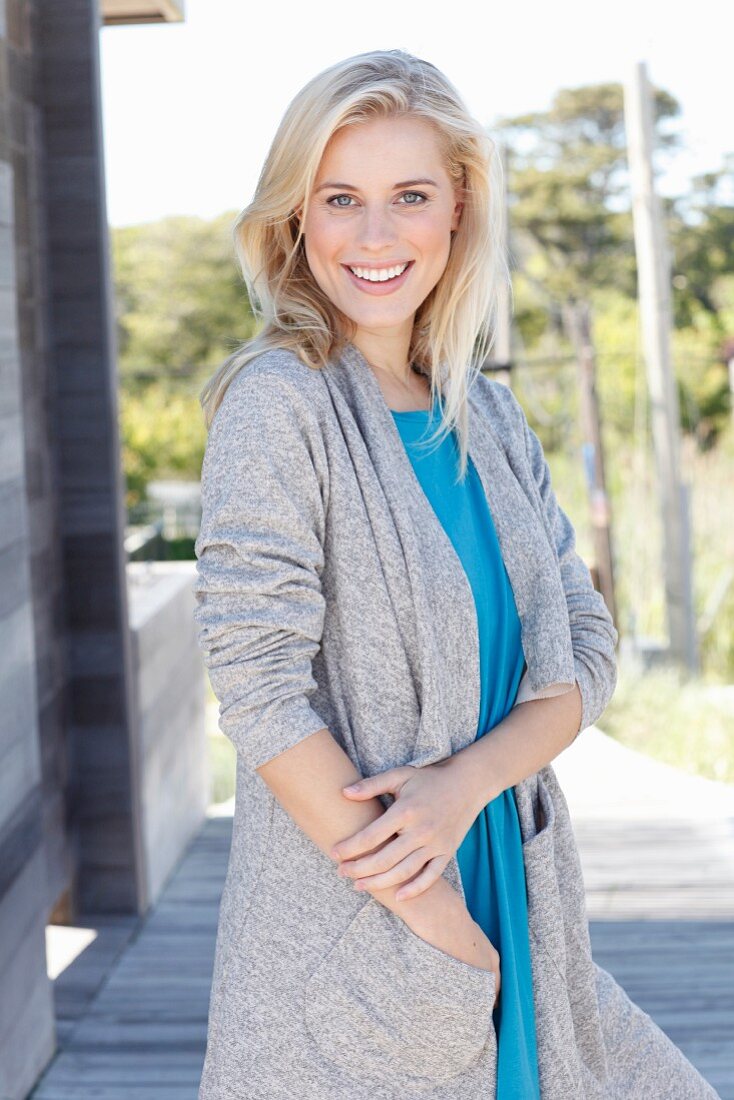 Junge blonde Frau in blauem Top und grauem Shirtmantel