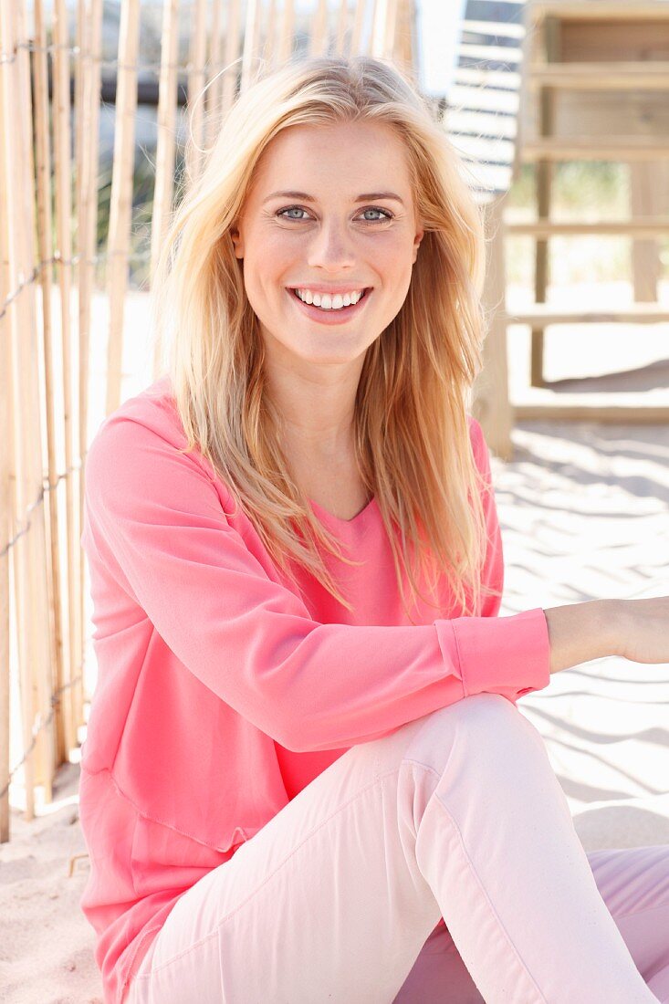 A young blonde woman wearing a long-sleeved, layer-look top and pink trousers