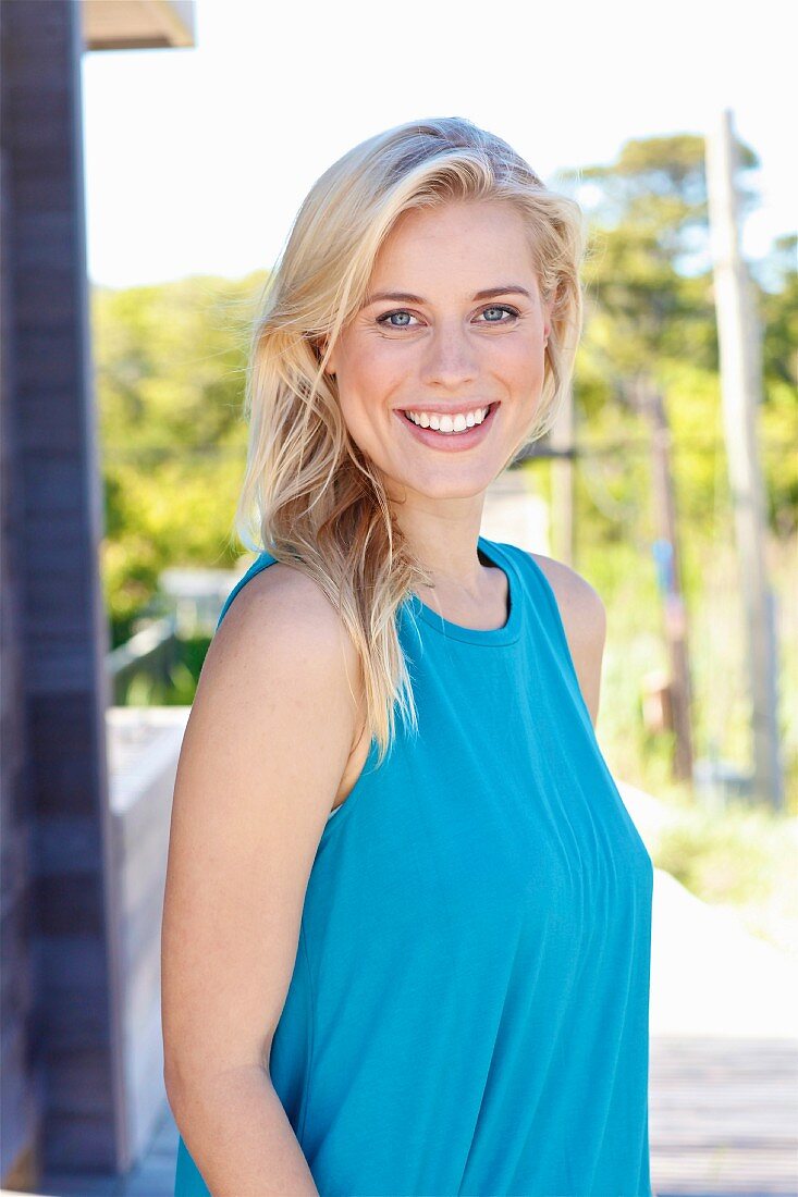 A young blonde woman on a beach wearing a blue top