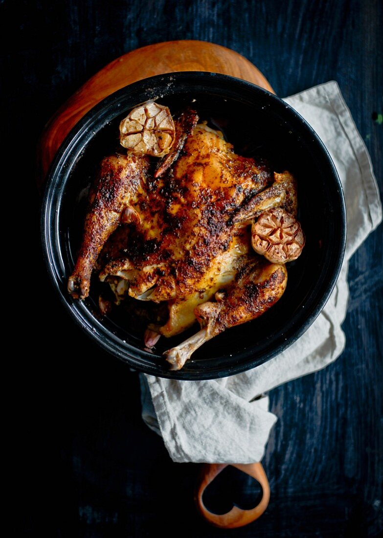 A whole roast chicken with garlic in a roasting dish