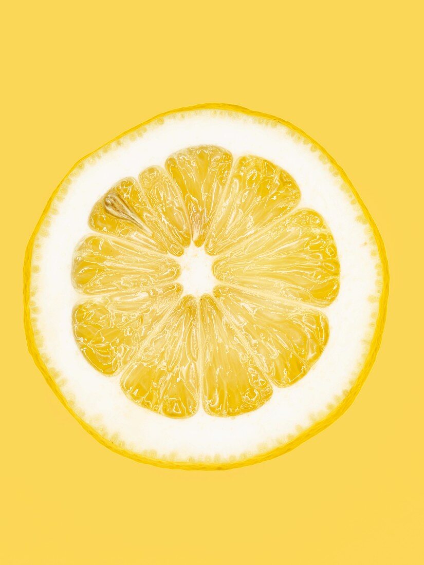 Aufgeschnittene gelbe Zitrone vor gelbem Hintergrund, Close-Up