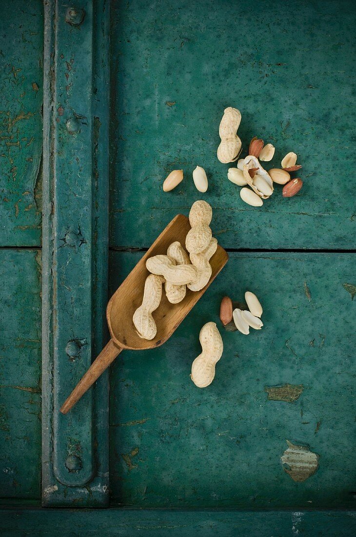 Peanuts, shelled and unshelled, on a wooden scoop on a rustic wooden surface