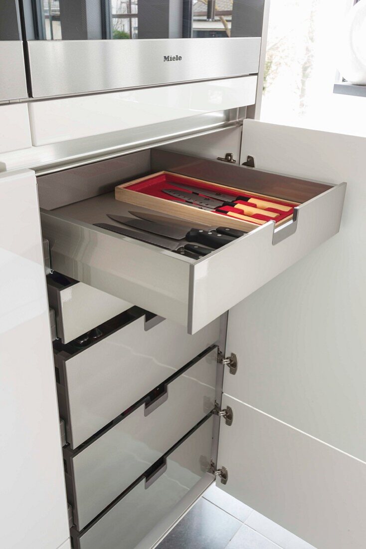 An open kitchen cupboard and drawers with a view of a knife collection