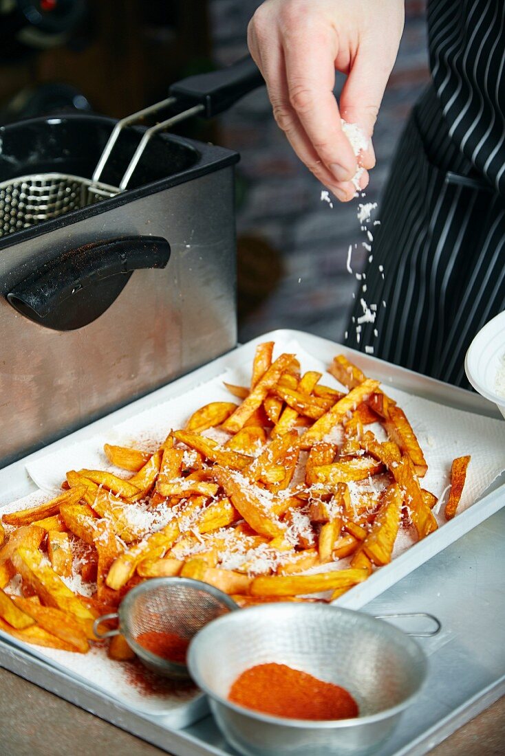 Sweet potato chips being seasoned with paprika and sea salt