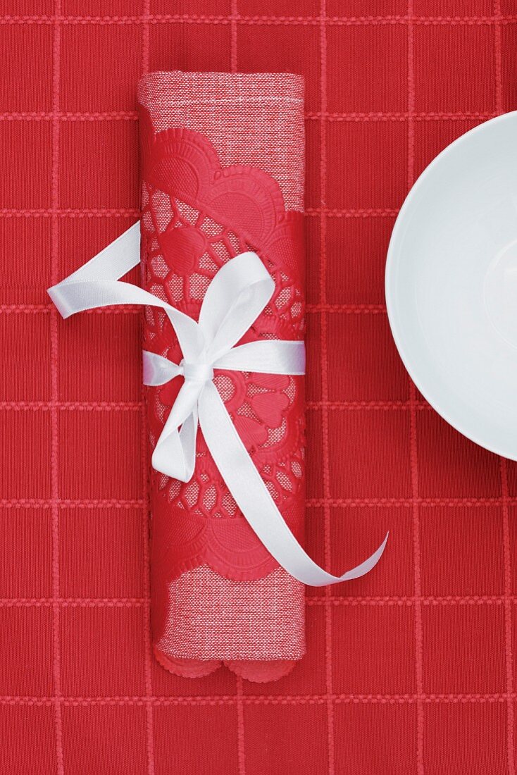 Red linen napkin and lace doily tied with white ribbon on red tablecloth