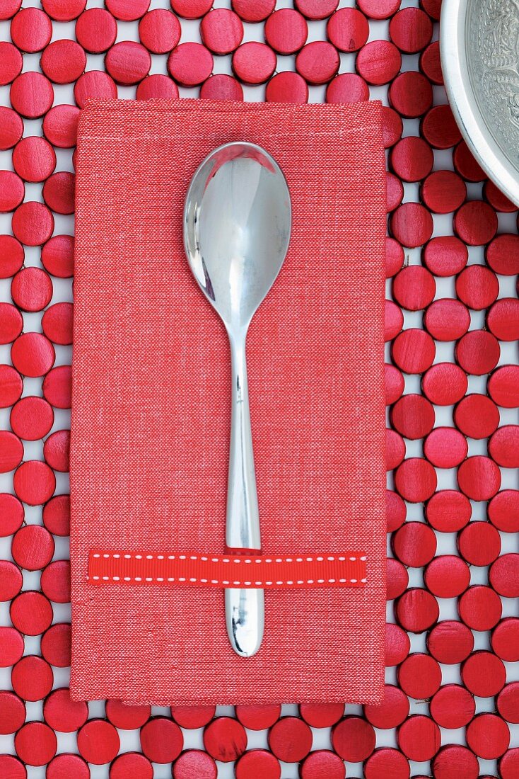 Löffel auf roter Stoffserviette und Tischset aus rotlackierten Holzplättchen