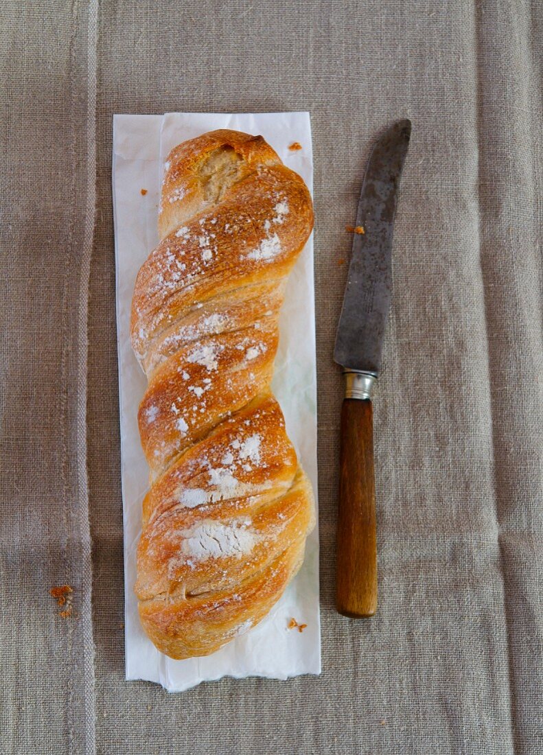 A loaf of twisted bread on a paper bag next to a knife