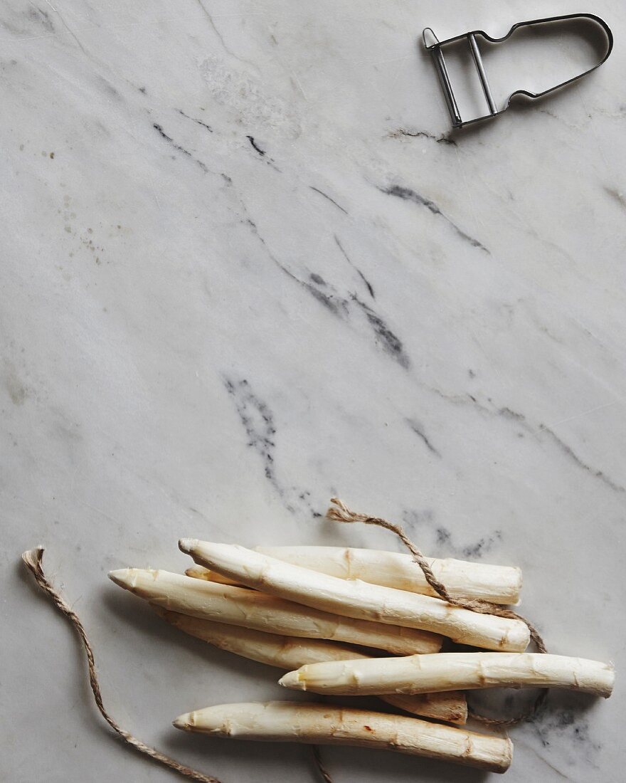 White asparagus spears, kitchen twine and a peeler