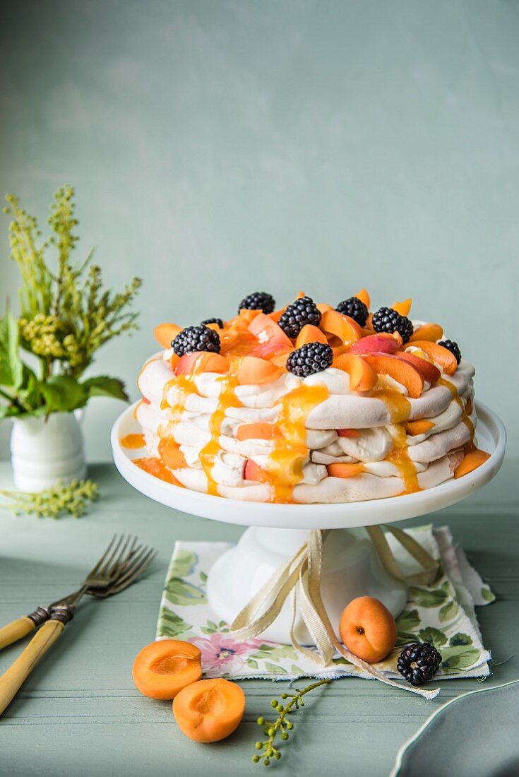 Apricot pavlova with apricot sauce and blackberries on a white cake stand