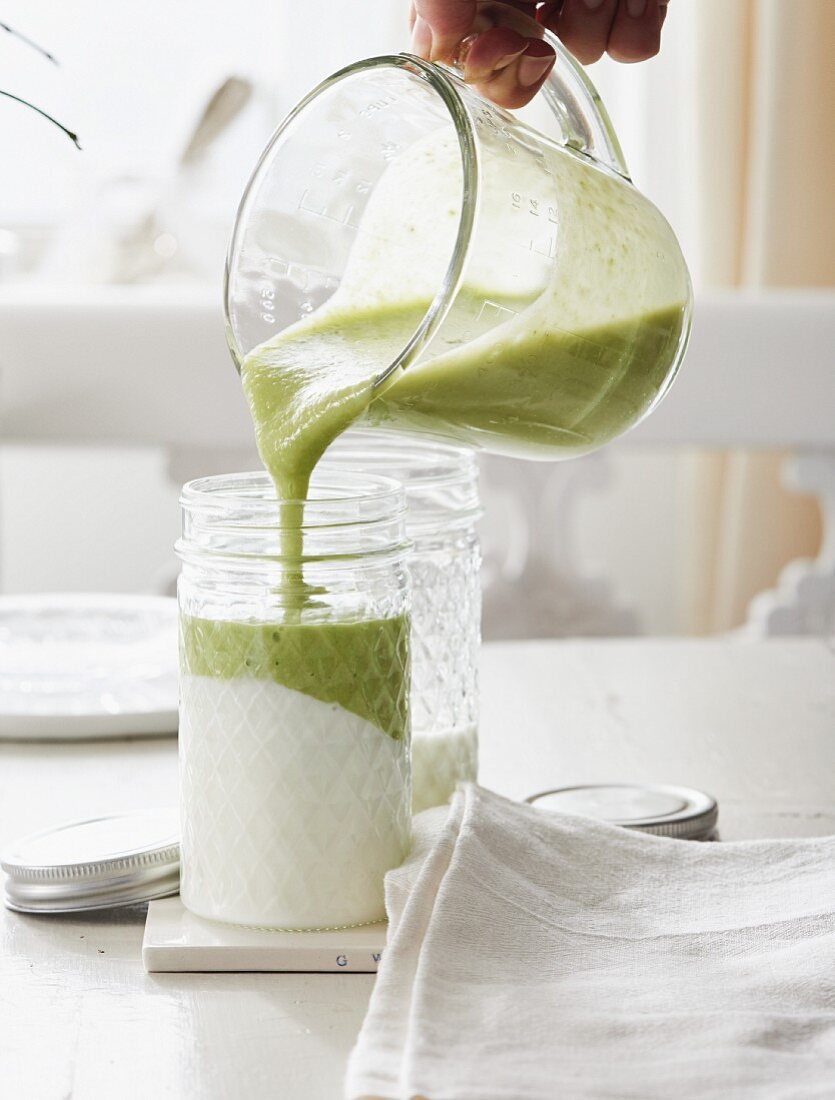 Grüner Smoothie mit Avocado und Matcha wird auf Joghurt in Glas gegossen