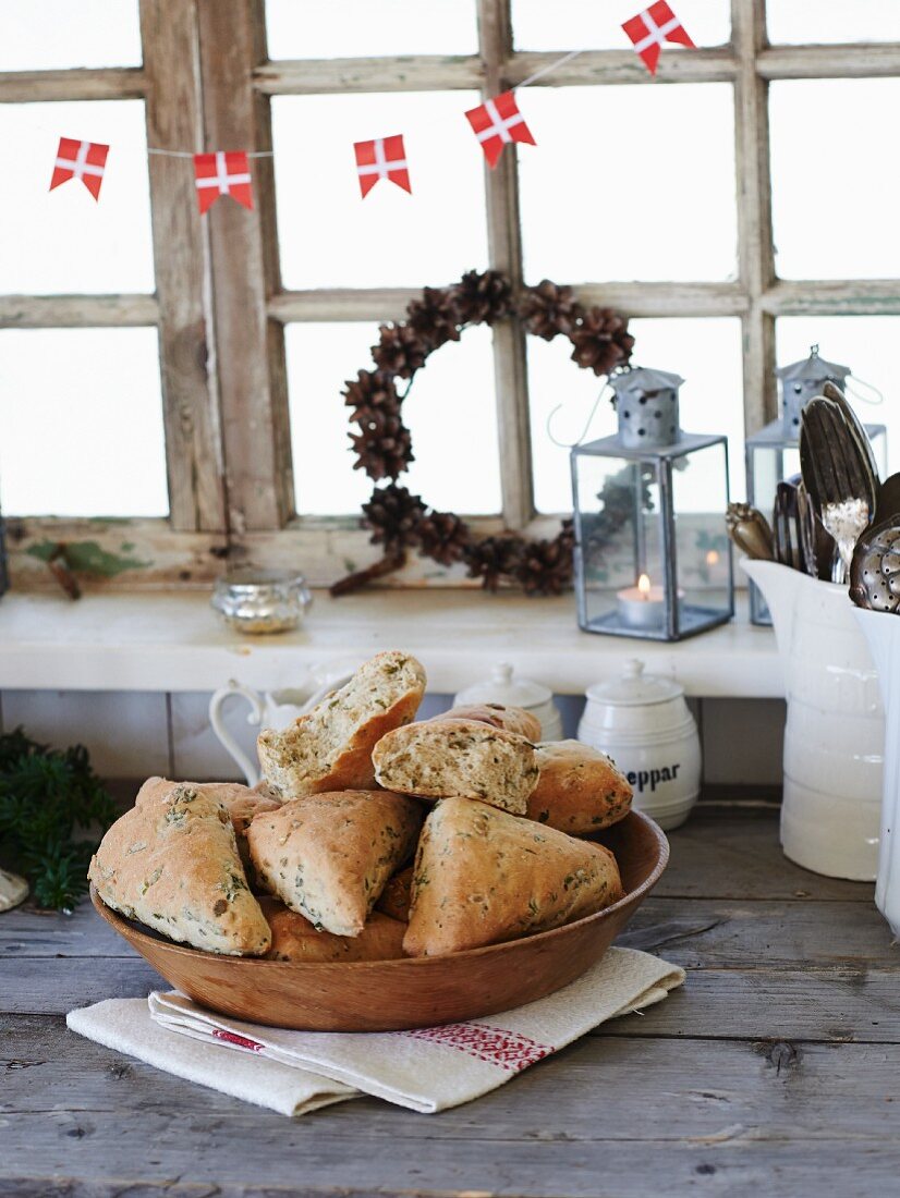 Homemade herb rolls in a wooden bowl in front of a kitchen window