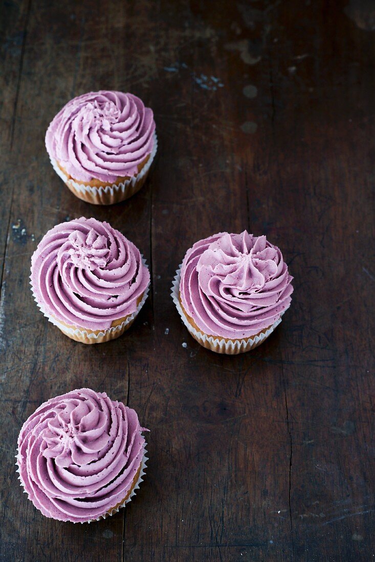 Four blueberry cupcakes on a dark wooden table