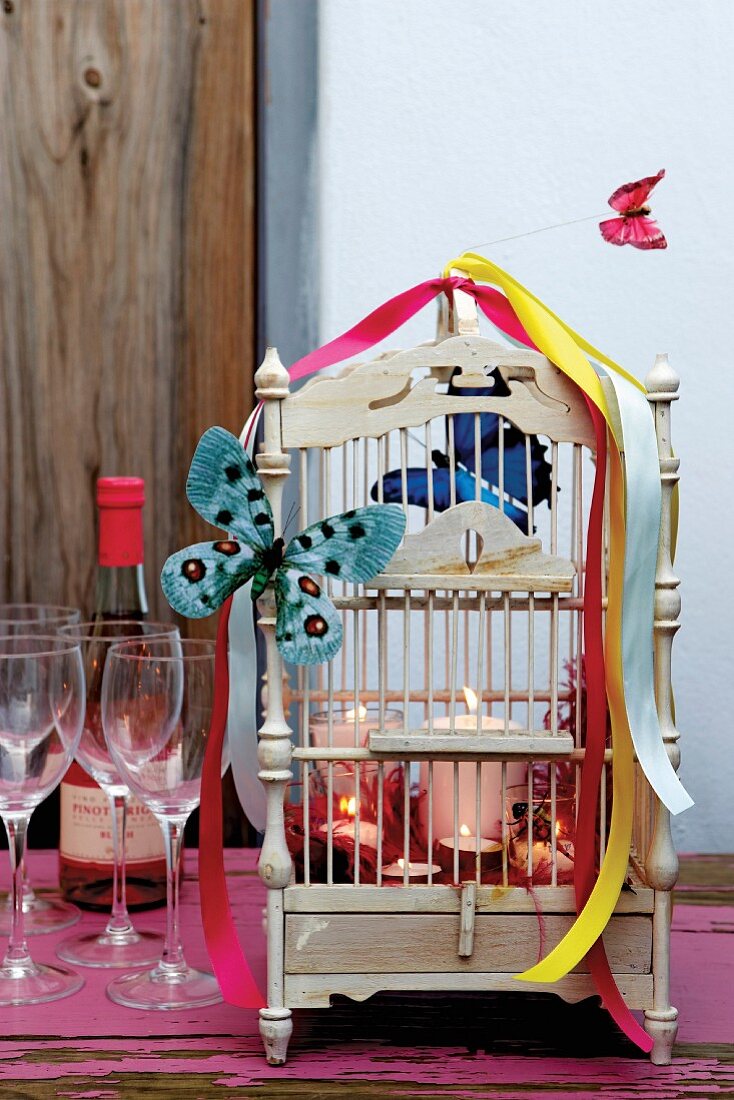 Verzierter Vintage Käfig mit Deko-Schmetterling, farbigen Schleifenbändern und brennenden Kerzen