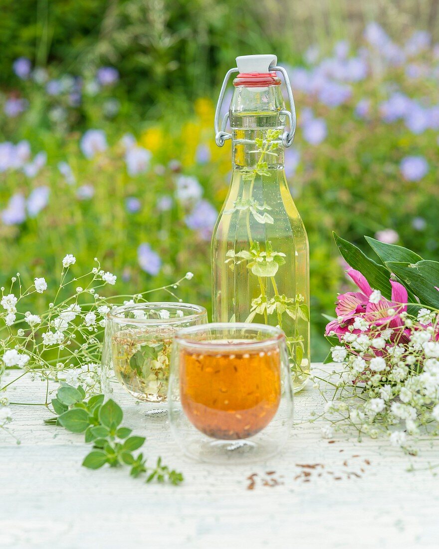 Selbstgemachtes Kräuteröl und Blumen auf Gartentisch