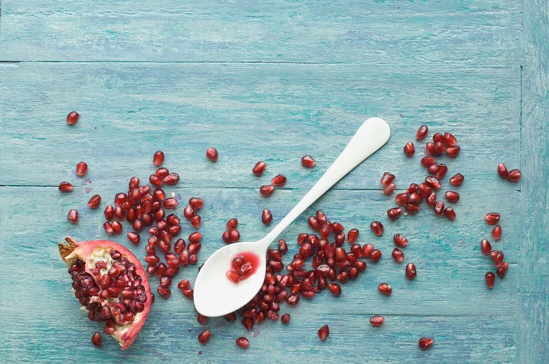 A spoon with pomegranate seeds and a piece of pomegranate on a wooden surface