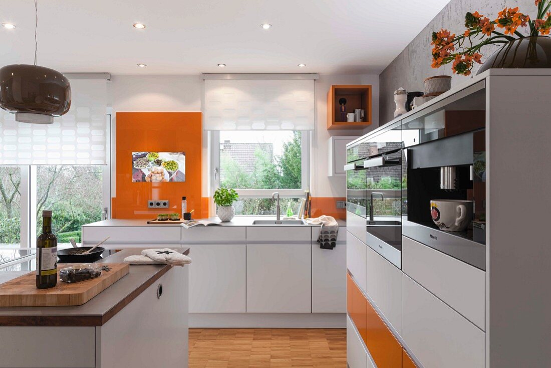 A modern, open-plan kitchen in white with orange accents