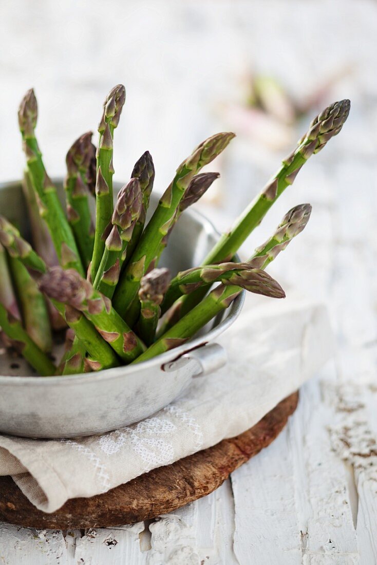 Green asparagus in a metal bowl on a linen cloth on a wooden board