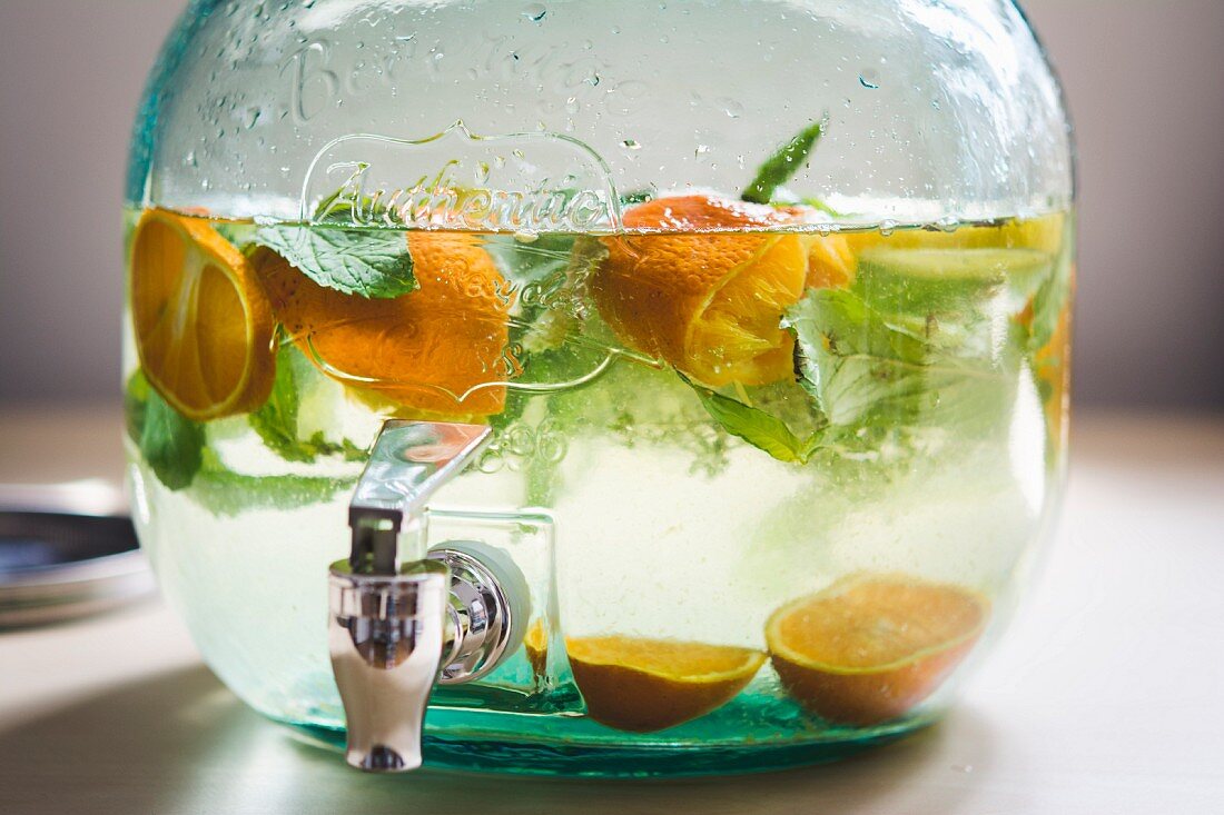 Sommerbowle mit Orangen und Minze in großem Glas mit Auslauf